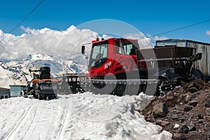 Red snowcat transport on white snow cleans ski track near mountain shelter. Caucasus Mountain