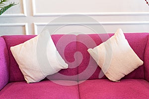 a red sofa with 2 cream colored pillows and white wall background
