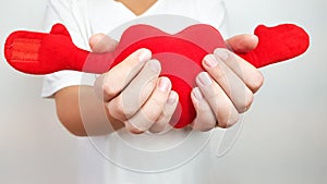 a red soft heart in the hands of a teenager on a light background. to give love