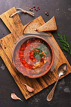 Red soup with beef borsch served in a clay plate with rye bread on a cutting board, top view. Russian food