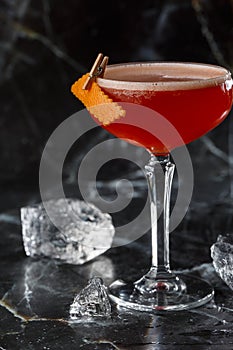 A red sour cocktail in a coupe glass garnished with an orange peel. Clover club with imported gin.