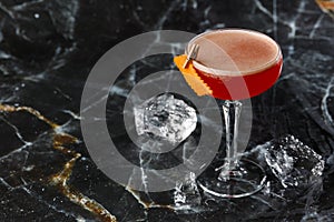 A red sour cocktail in a coupe glass garnished with an orange peel. Clover club with imported gin.