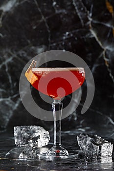 A red sour cocktail in a coupe glass garnished with an orange peel. Clover club with imported gin.