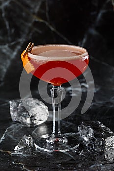 A red sour cocktail in a coupe glass garnished with an orange peel. Clover club with imported gin.