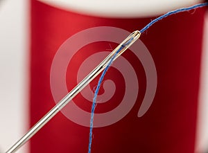 Red spool of thread with a gold colored needle that has been threaded