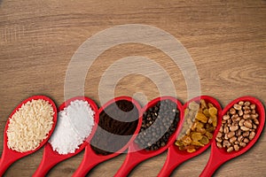 Red spoons with grains and spices, on a wooden background.top wiew