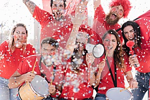 Red sport fans screaming while supporting their team out of the stadium - Focus on right girl with drum