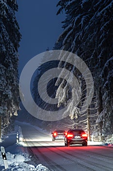 red sports car driving along a snow covered country road at night