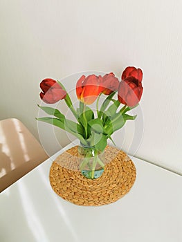 Red spring tulips on a white table on a wicker placemat. Minimalist composition with flowers.