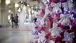 Red spruce in silver bows. New Year`s and abstract blurred shopping mall background with Christmas tree decorations.