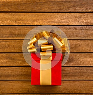 Red Square Gift Box with Gold Ribbon and Big Loopy Bow on it. Copy Space. Wooden Background