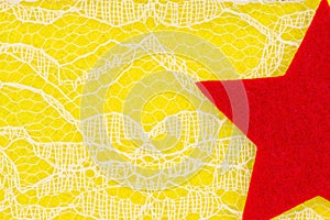 Red star with delicate lace textured material on bright yellow knit background