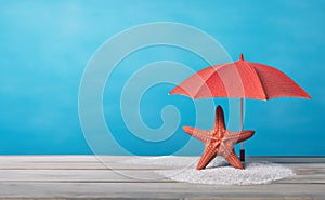 Red starfish and beach umbrella on the white sand and rustic table over blue background