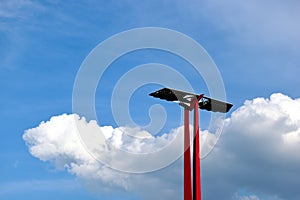 Red steel light poles in low angle view with flat PV solar panels on top