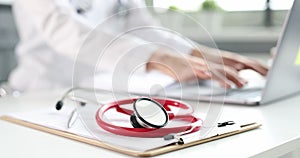 Red stethoscope and documents lying against background of doctor typing on keyboard of laptop closeup 4k movie slow