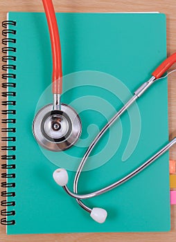 Red stethoscope lying on a thin green book.