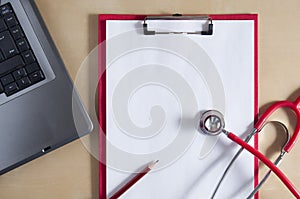 Red stethoscope and red pencil on a red clipboard. Near laptop. Medical device. Top view. Treatment, health care. Heart
