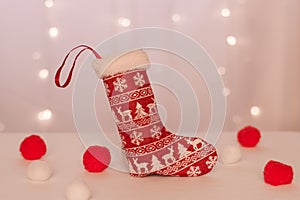 Red stocking with deer for handmade gifts stands against the background of Christmas lights and soft balls