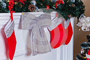 Red stockings and silver shiny decorative bow hanging on fireplace with fir branches. Merry Christmas, Happy New Year and winter