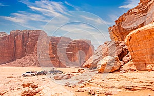 Red stones and rocks of Wadi Rum desert with cars in background, Jordan