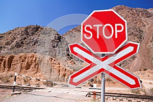 Red Stop sign at a deserted railroad crossing nestled amidst barren, empty terrain against blurred red mountains