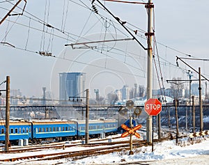 Red stop sign at the railway crossing against the background of the railway station and buildings of the winter city