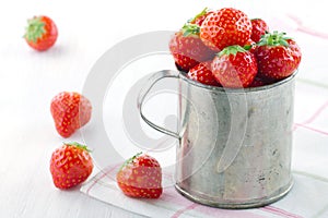 Red strawberries in an old metal measurement cup