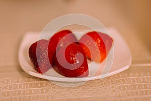 Red strawberries on a white saucer on the table.