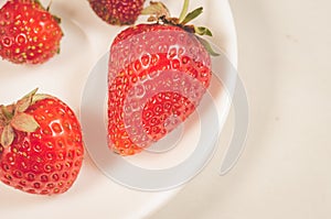 red strawberry berries in a white bowl/red strawberry berries in a white bowl on a white table closeup. Top view
