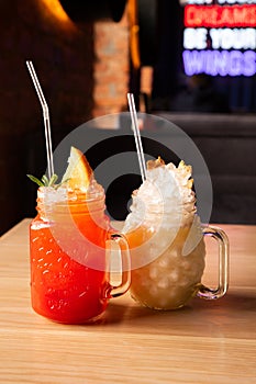 Red Strawberry lemonade with soda, ice, cocktail tube and orange slice in glass with handle. Cocktail Pina Colada with ice,