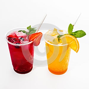 Red strawberry and yellow orange cocktail with ice cubes decorated with mint and slices of fruits. Close-up, on a white