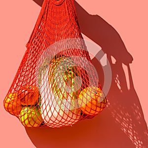 Red string bag with vegetables and fruit on a pink background. The concept of zero waste