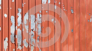 Red striped galvanized corrugated roofing sheet with peeling paint. The texture is made of old silver steel corrugated iron with a