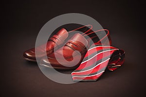 Red striped rolled necktie and brown men`s shoes. Selective focus