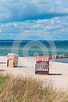 Red striped roofed chairs on empty sandy beach in Travemunde. Grass bush in foreground. Germany