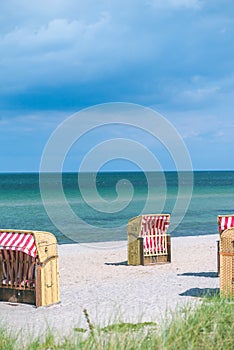 Red striped roofed chairs on empty sandy beach in Travemunde. Grass bush in foreground. Germany