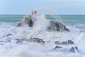 Red structure of beacon on North Rock ar base of Mount Maunganui with wild stormy sea crashing around and over it