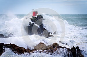Red structure of beacon on North Rock ar base of Mount Maunganui with wild stormy sea crashing around and over it