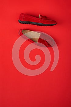 Red suede woman`s mocassin shoes over red background