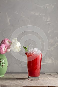 Red summer cocktail with juice, cruched ice and fresh flowers on the table