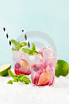 Red Summer cooling drink with ice, lime, raspberries and syrup on light background.