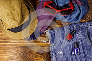 Red sunglasses, straw hat, summer scarf, jeans shorts and nail polish on wooden background