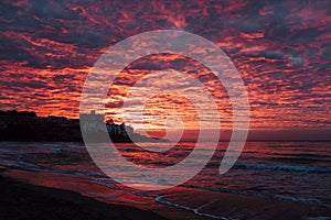 Red sunset at the beach with town in silhouette and dramatic sky with clouds. Amazing sunlight sunrise seascape with waves and