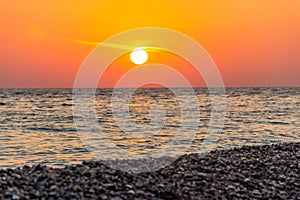 Red sunset on the sea beach. Soft sea waves and sea pebbles. Composition of nature