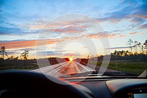 Red sunset view with shining sun from the car front window. Driving car during sunset concept. View on nature landscape and a road
