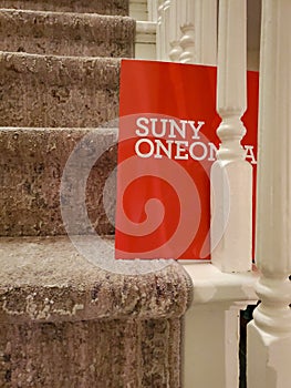 Red SUNY ONEONTA file folder standing on end between rungs on carpeted stairs