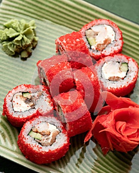 Red Sushi roll in masago or tobiko caviar on green background. Inside-out Sushi Set. Red on green, Bright colors