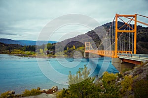 Red suspension bridge over the water runoff of General Carrera Lake, near Lake Bertrand, Puerto Tranquilo, Chile Chico, Aysen,