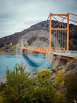 Red suspension bridge over the water runoff of General Carrera Lake, near Lake Bertrand, Puerto Tranquilo, Chile Chico, Aysen,