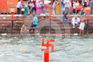 Red swastika cross on the Ganges River at Haridwar, India, sacred city for Hindu Religion. Pilgrims bathing on the ghats.